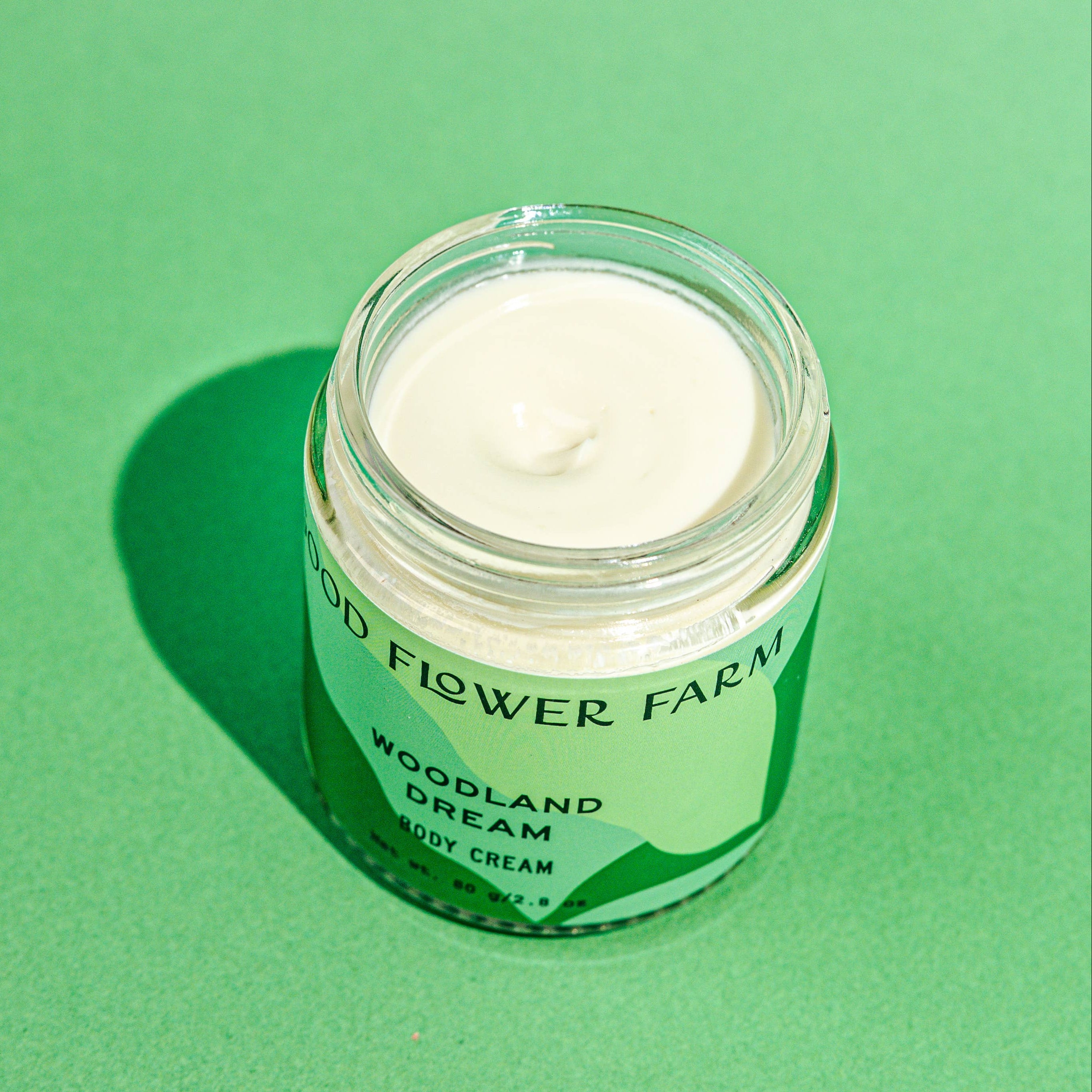 Jar of body cream labeled 'Woodland Dream' on a green background