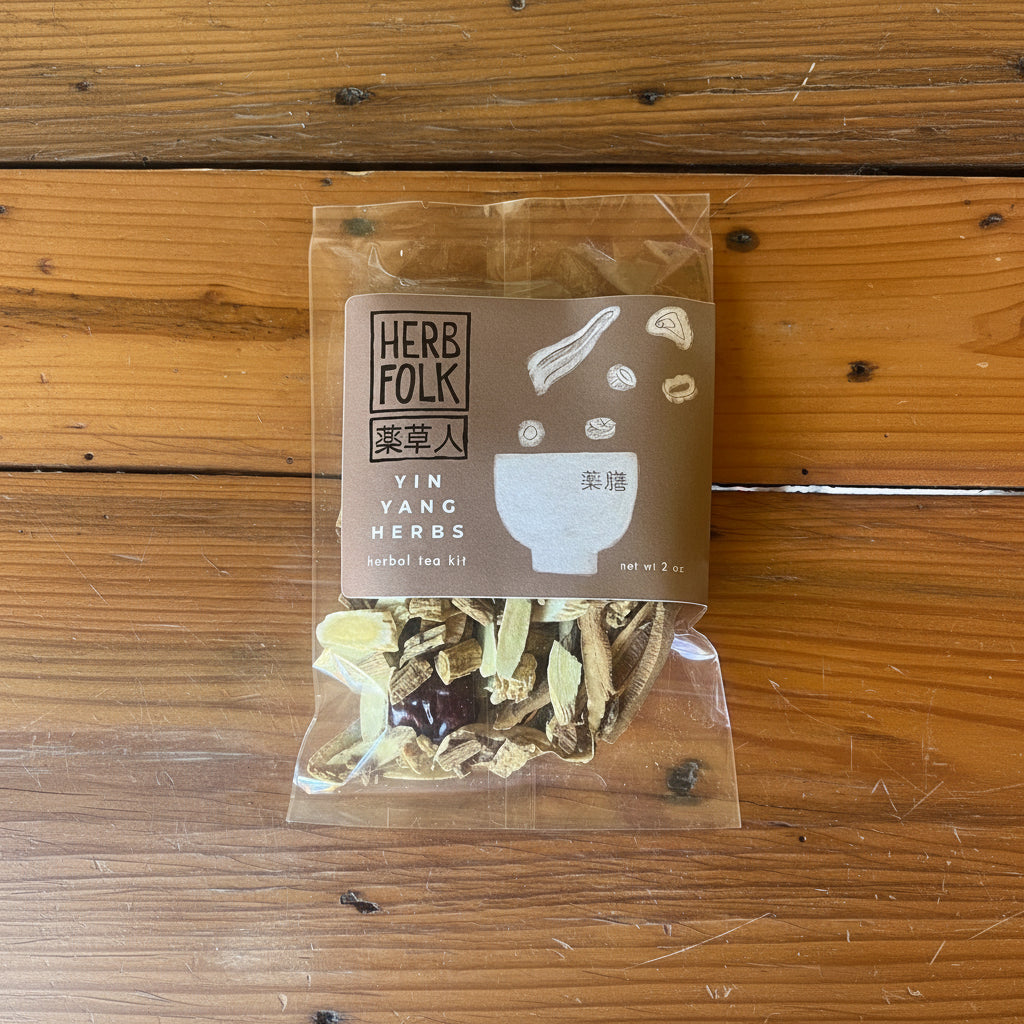 Packaged herbal tea kit with visible dried herbs through the clear plastic, labeled 'YIN YANG HERBS' on a wooden surface.