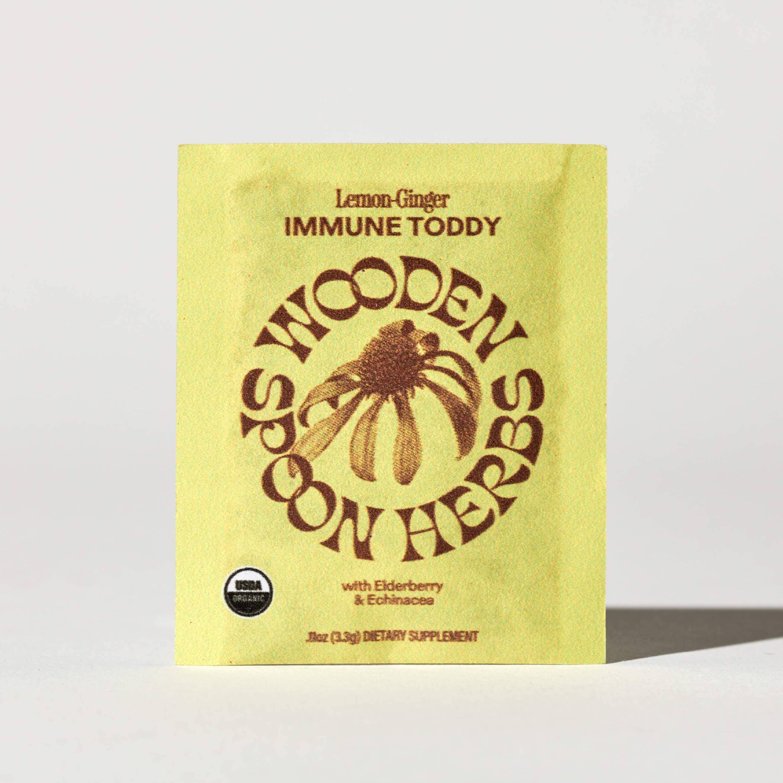 Yellow package of Wooden Spoon Herbs Lemon Ginger Immune Toddy on a light gray background