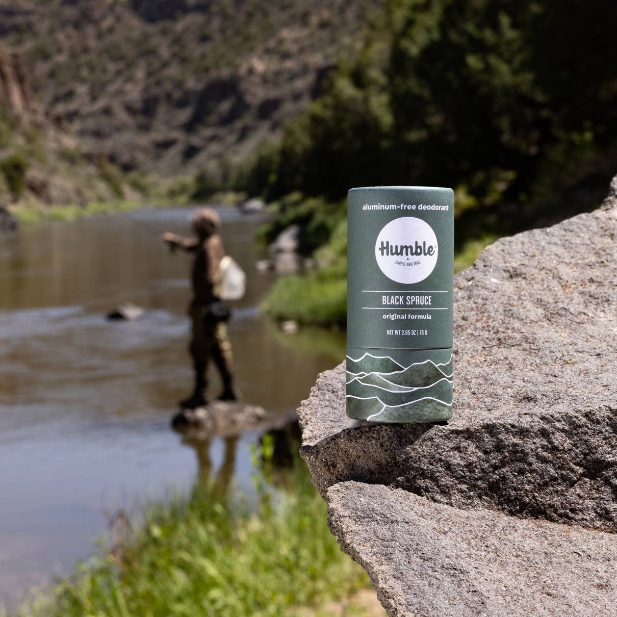 Humble deodorant stick on a rock with a person fishing in the background