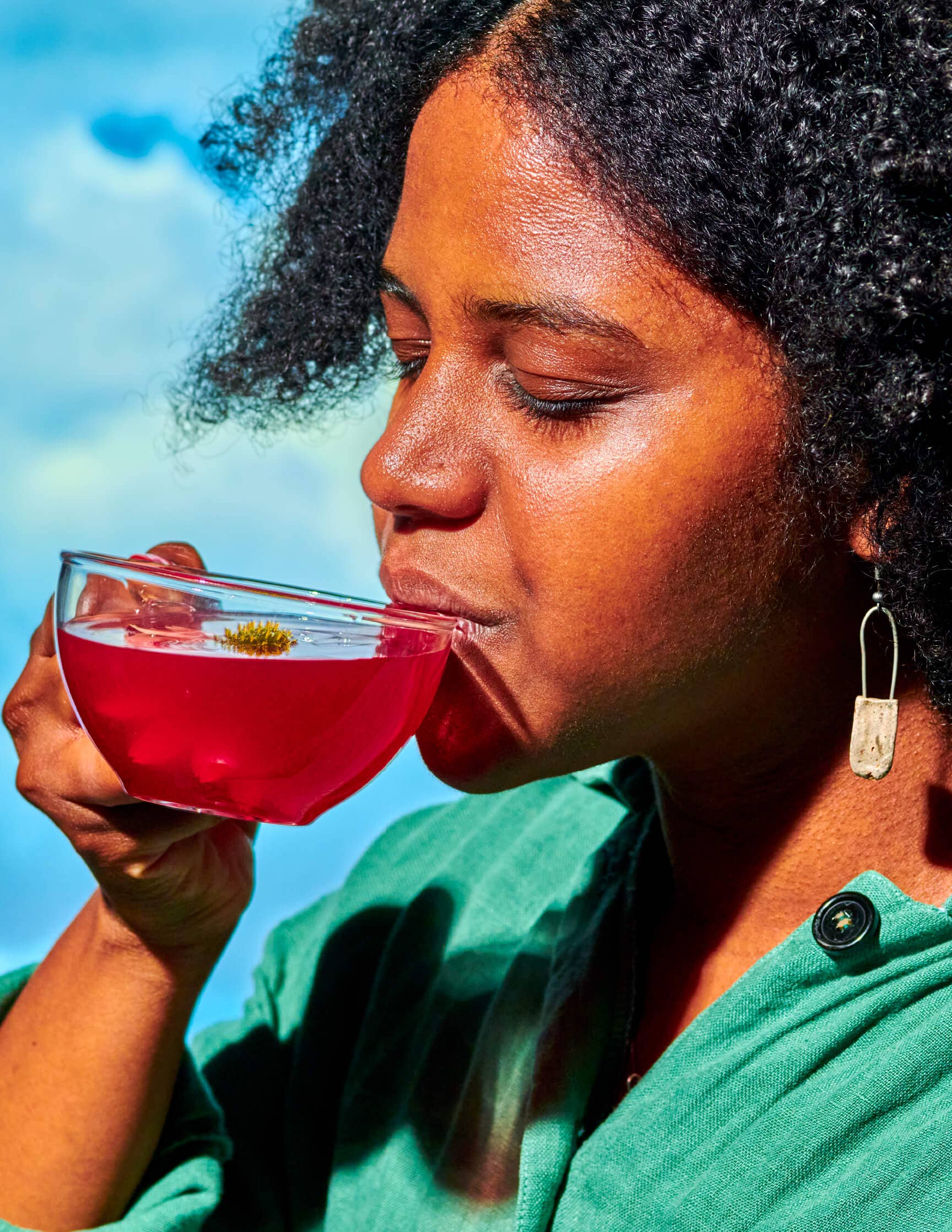 Woman drinking a pink beverage outdoors with a clear blue sky.