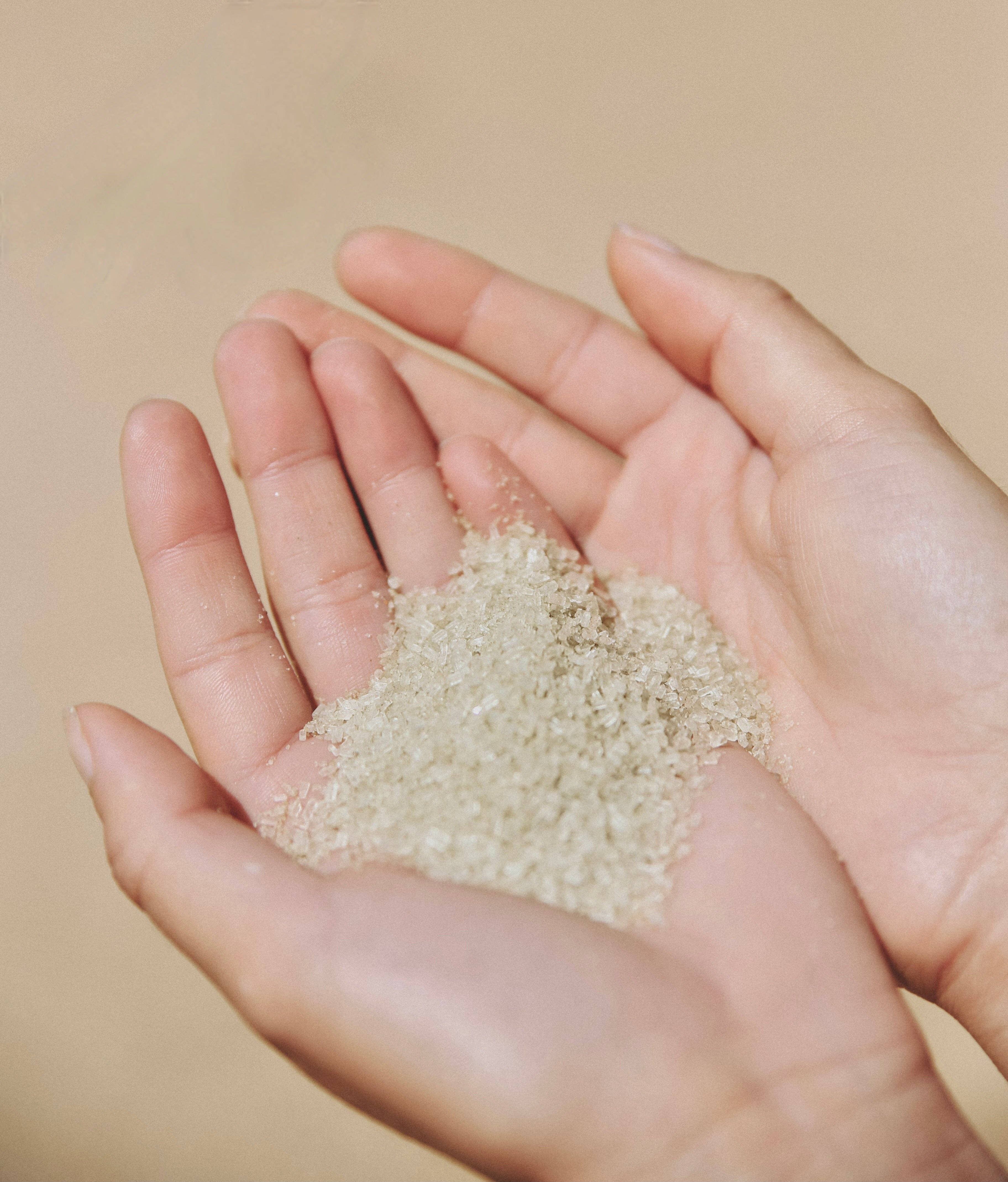Hand holding a small amount of light brown sugar against a beige background
