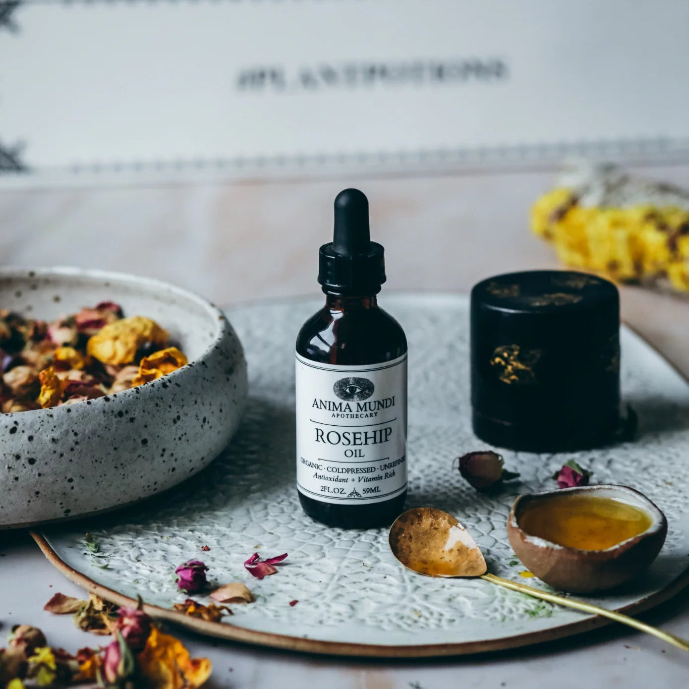 Anima Mundi Rosehip Oil bottle on a decorative plate with dried flowers and a candle.