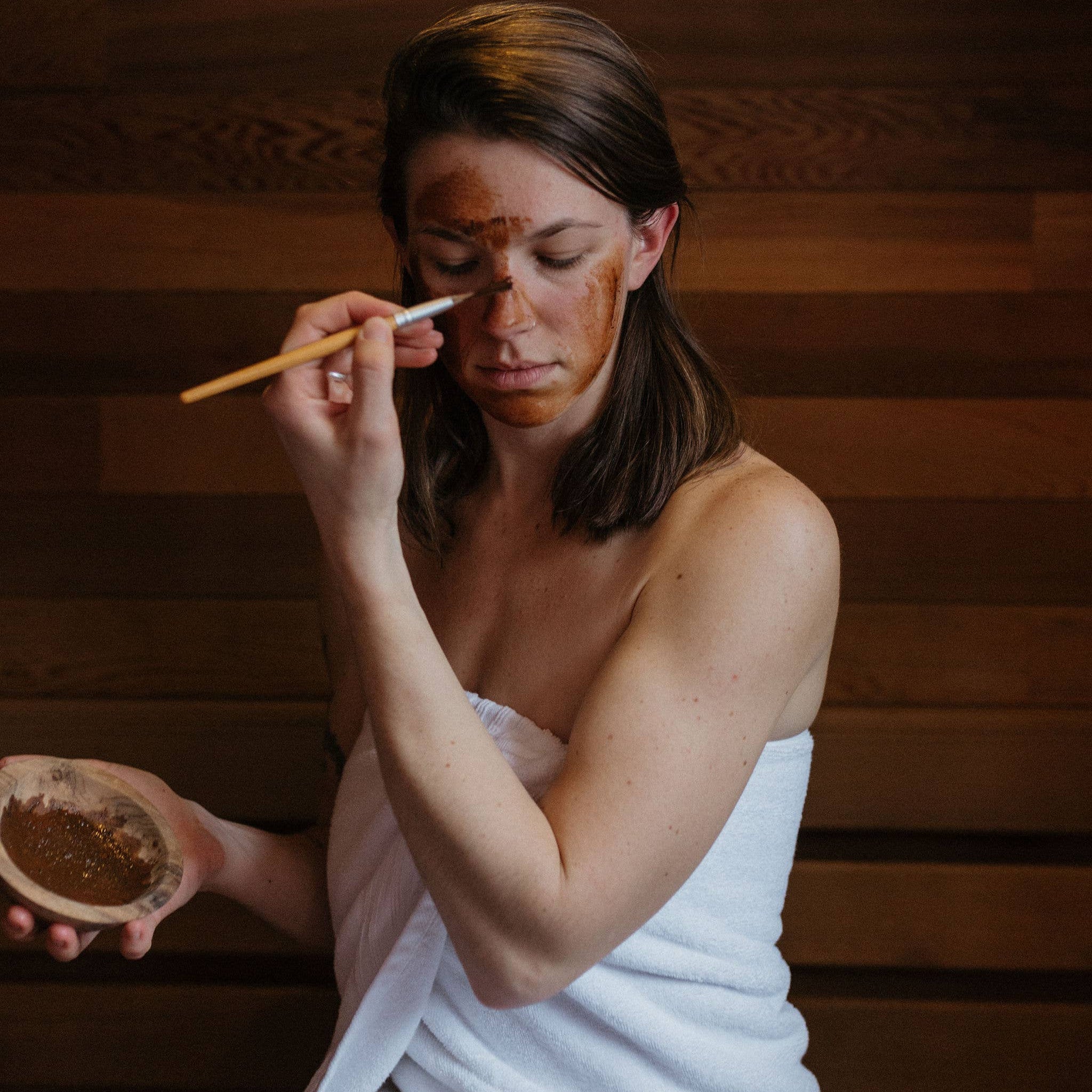 Woman applying a facial mask with a brush in a wooden room