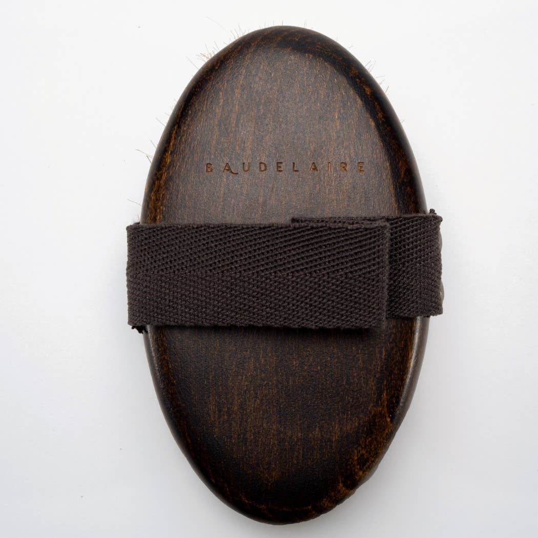 Wooden body brush with a strap on a white background, branded 'Baudelaire'.