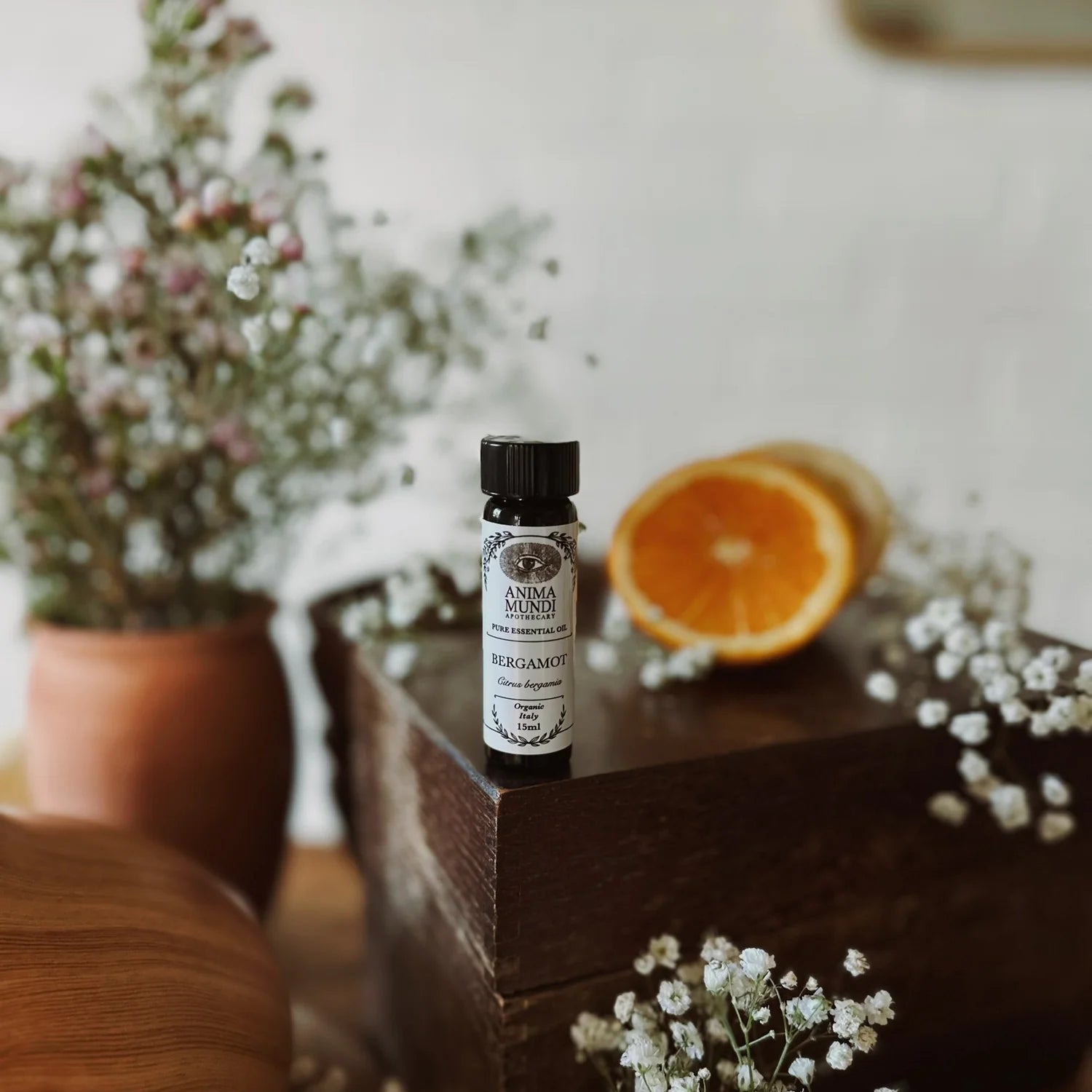 Small bottle of Anima Mundi oil on a wooden surface with oranges and flowers.