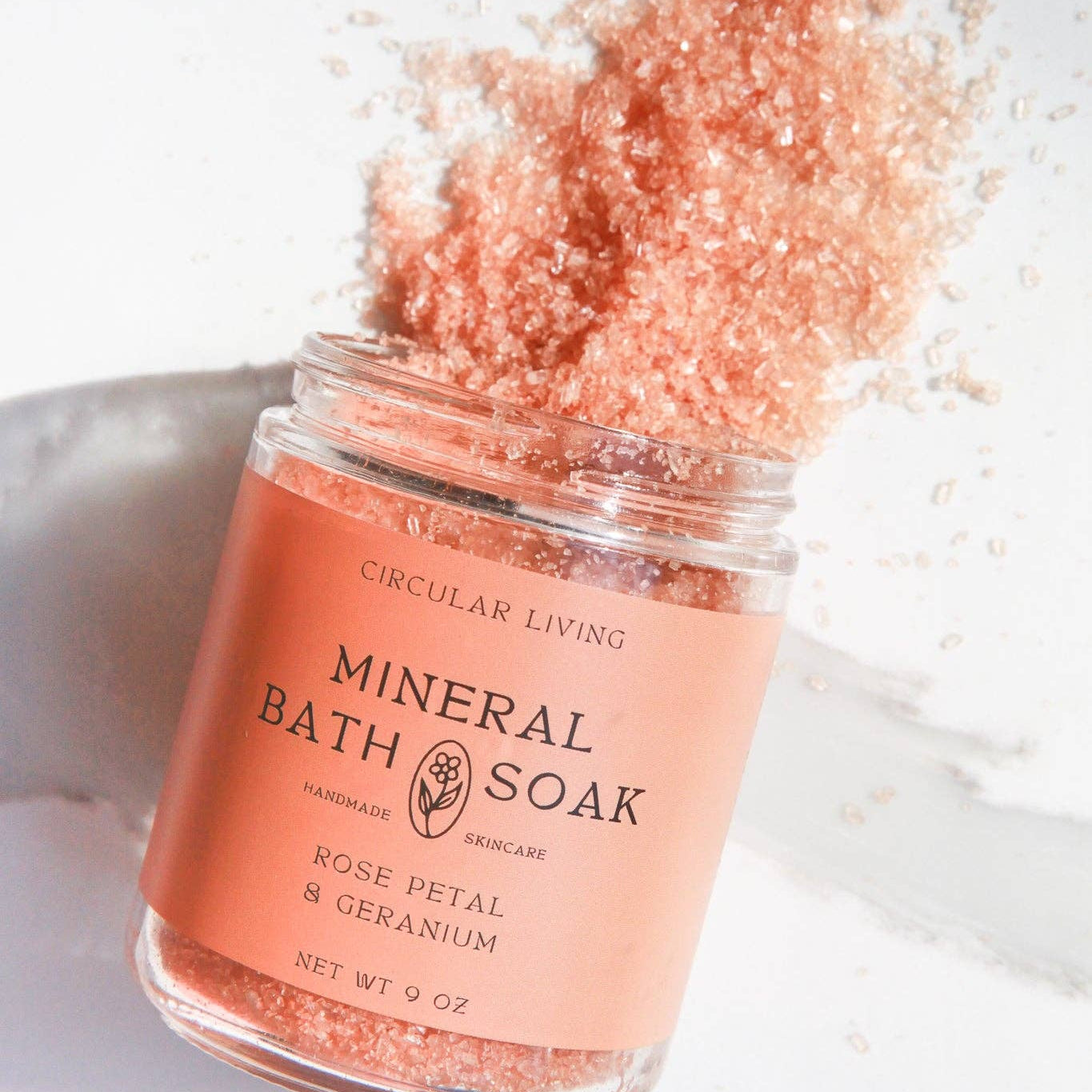 Jar of mineral bath soak with rose petal and geranium scent on a white background