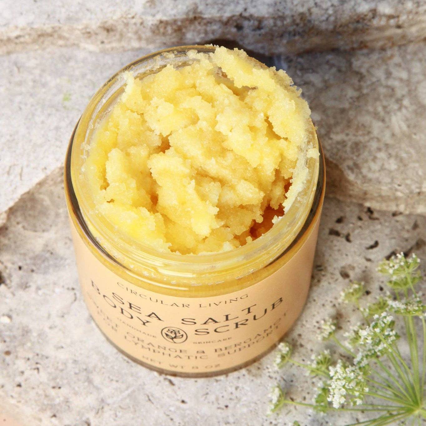 Jar of sea salt body scrub on a stone surface with flowers.