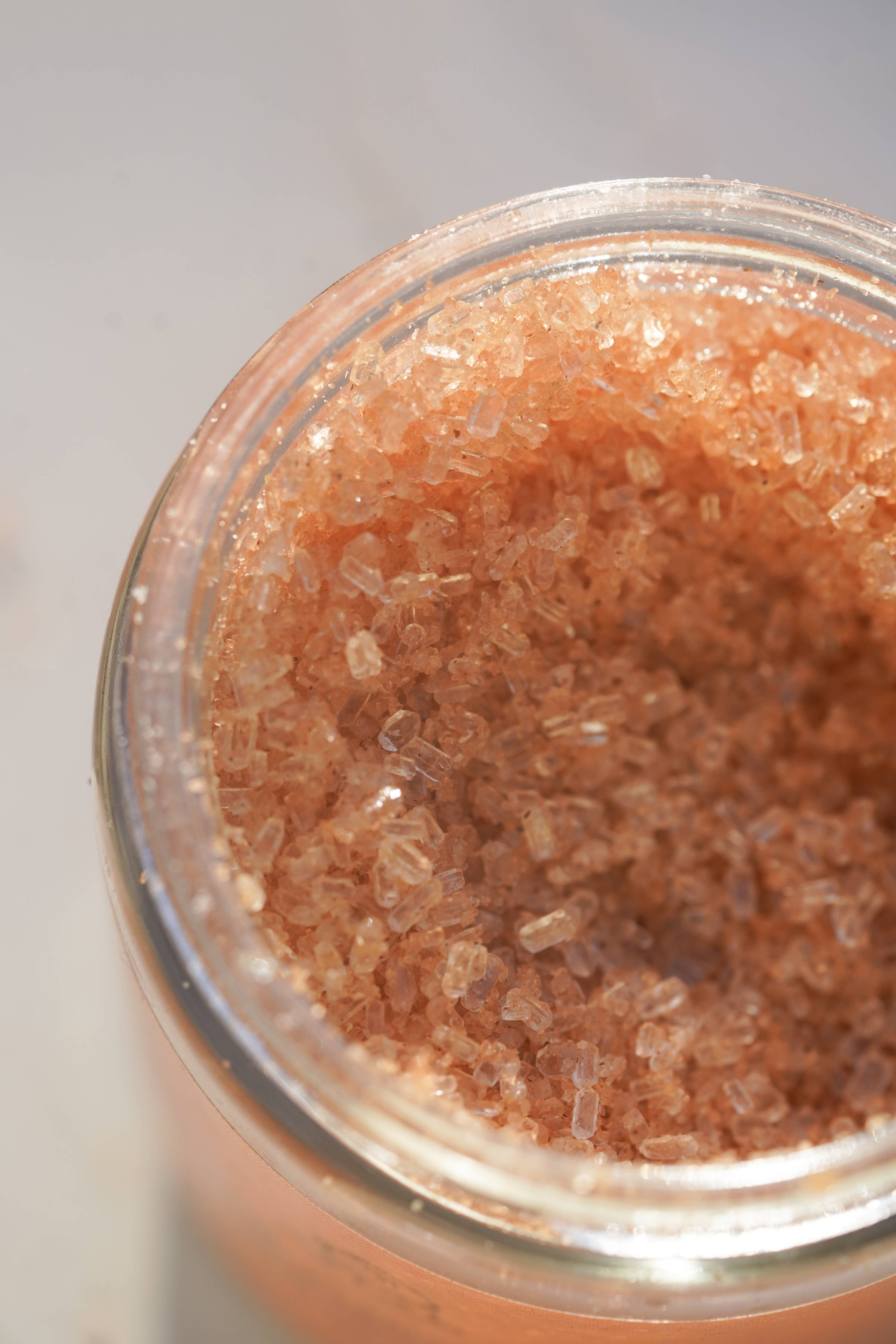 Close-up of a container with brown salt scrub crystals on a light gray background