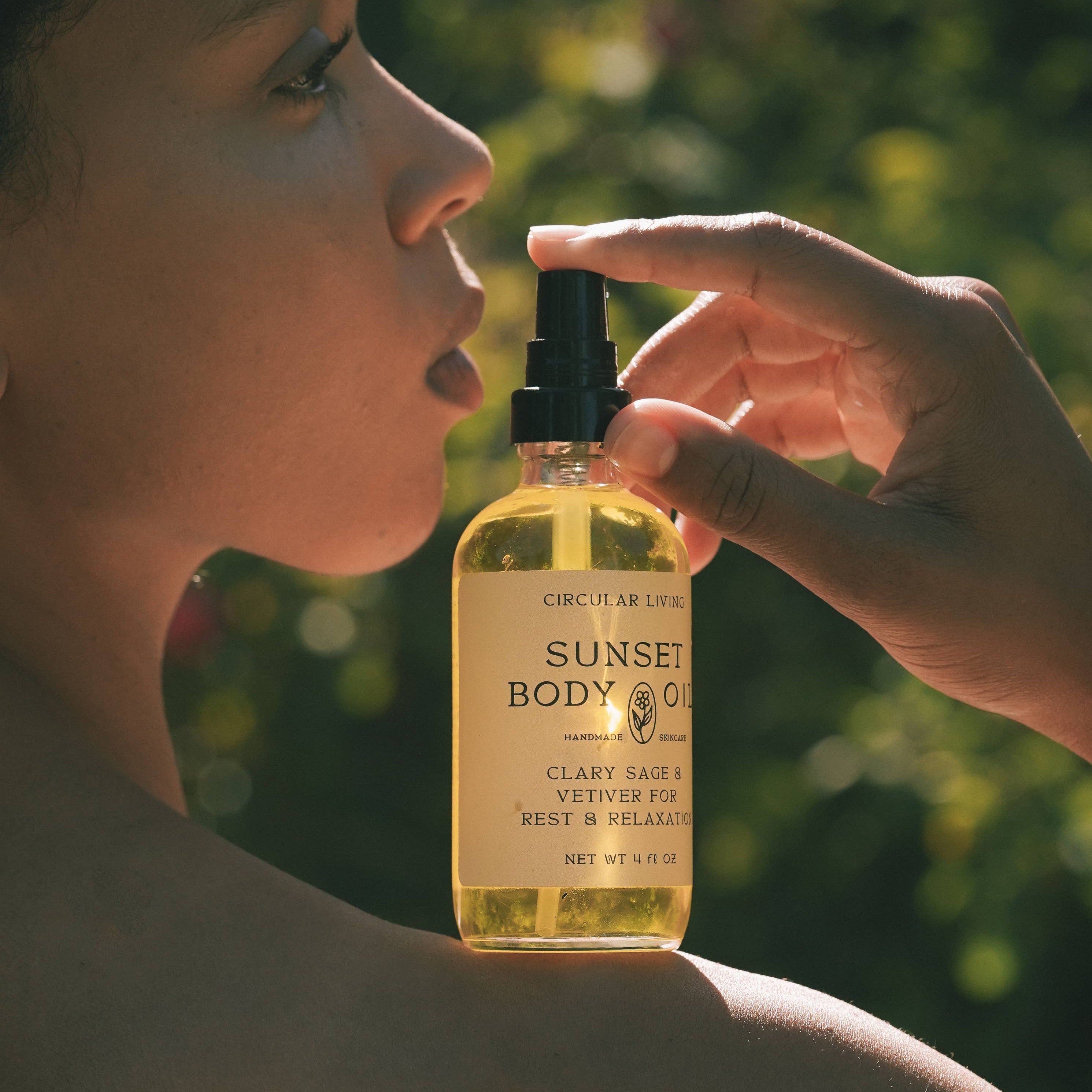 Person holding a bottle of Sunset Body Co. product close to their face with a blurred green background