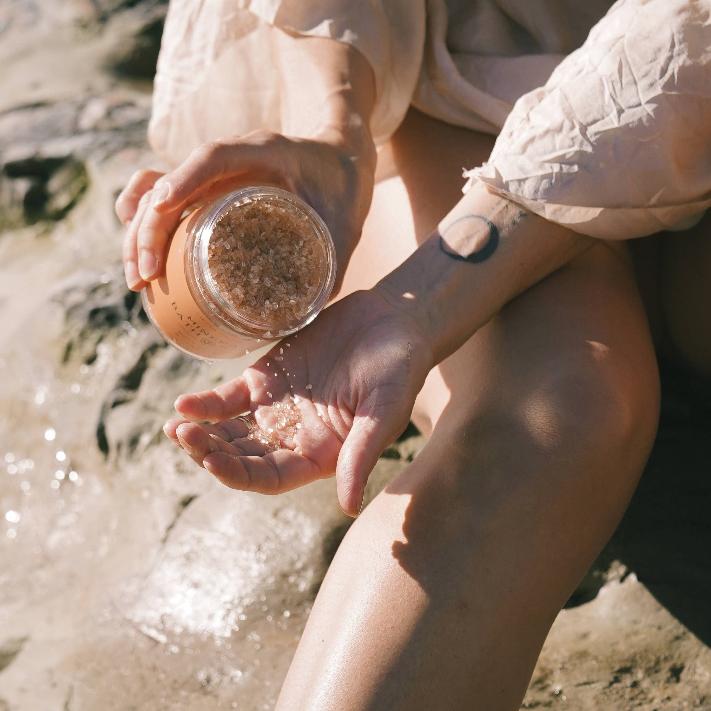 Person holding a jar of bath salt by a body of water