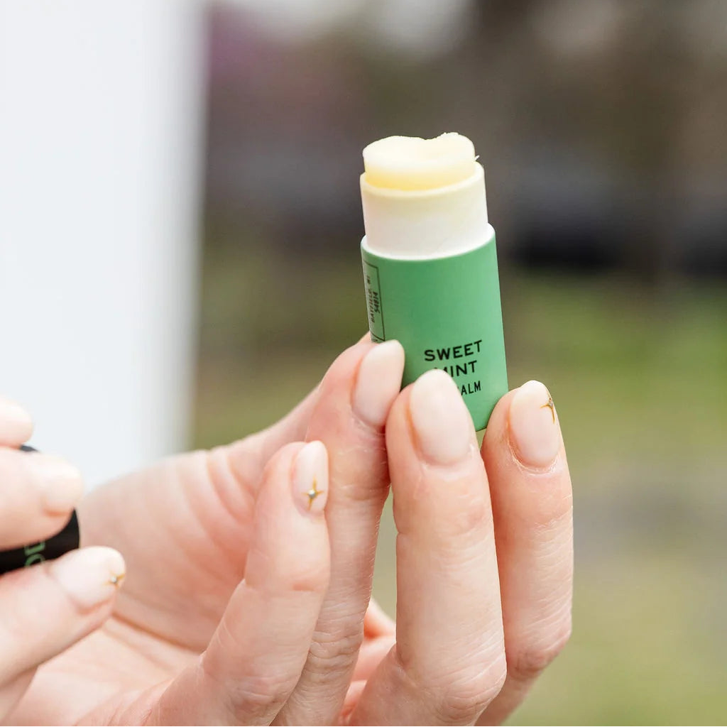 Hand holding a green lip balm with a blurred outdoor background