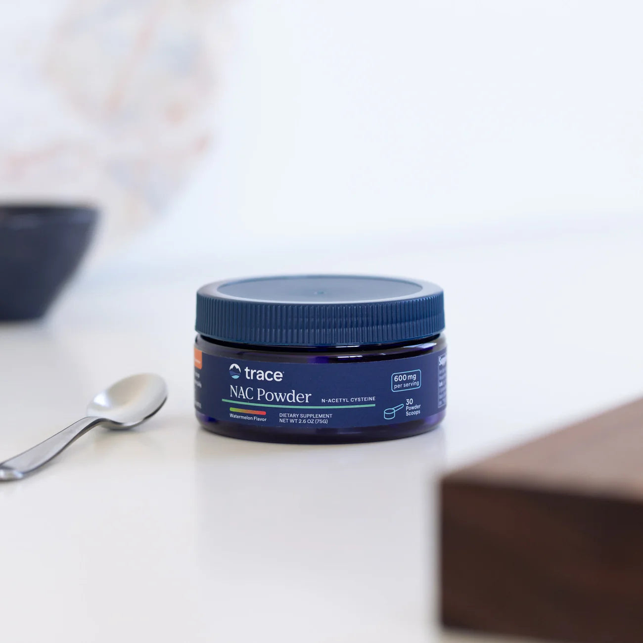 Jar of trace NAC Powder on a white surface with a spoon and blurred background