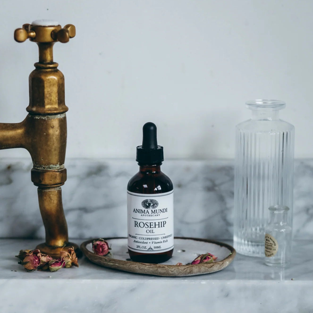 Bottle of Anima Mundi Rosehip Oil on a marble surface with a brass faucet.
