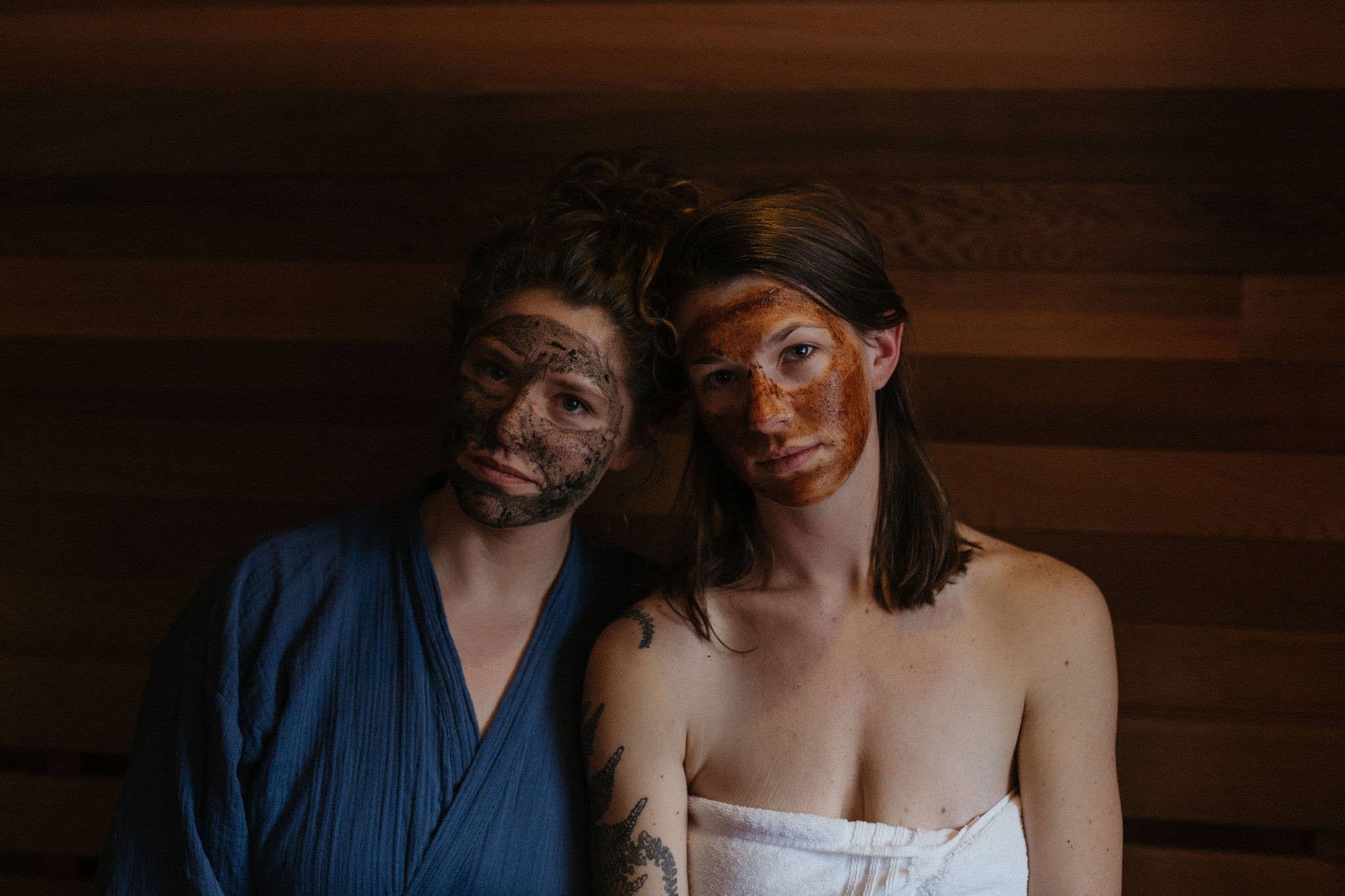Two people with mud facials sitting in a sauna.