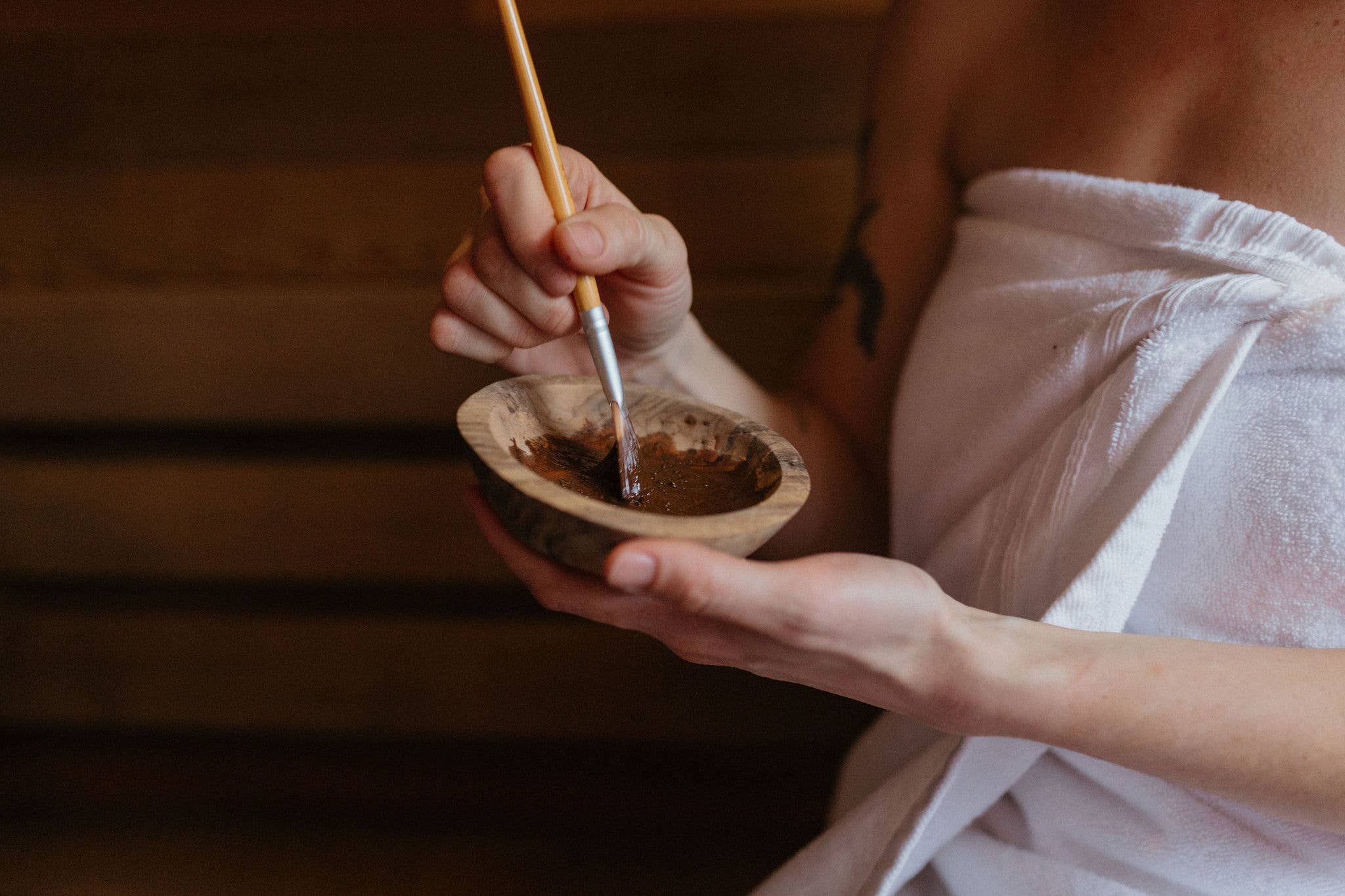 Person holding a small bowl with a wooden spoon, blurred background